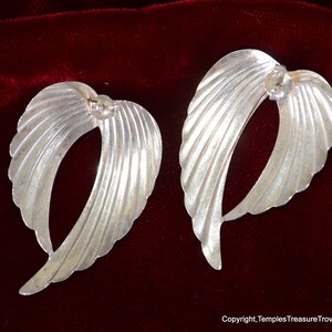 May include: A pair of silver earrings shaped like wings with a textured, ribbed design.