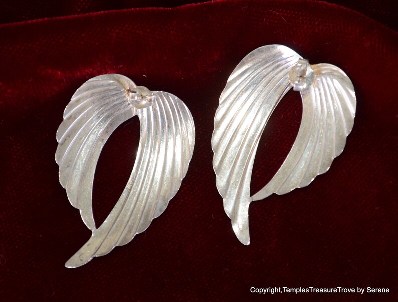 May include: A pair of silver earrings shaped like wings with a textured, ribbed design.