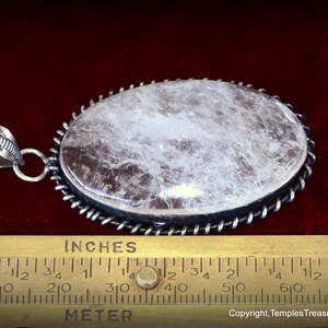 May include: A silver pendant with a large, oval-shaped, clear quartz stone. The stone has a cloudy, white appearance. The pendant is approximately 2 inches long.
