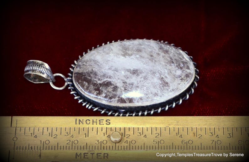 May include: A silver pendant with a large, oval-shaped, clear quartz stone. The stone has a cloudy, white appearance. The pendant is approximately 2 inches long.