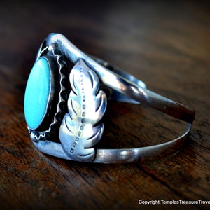 Puede incluir: Un brazalete de plata con una piedra turquesa y un dise&ntilde;o de pluma. El brazalete est&aacute; estampado con "OROBORO" en el lateral.