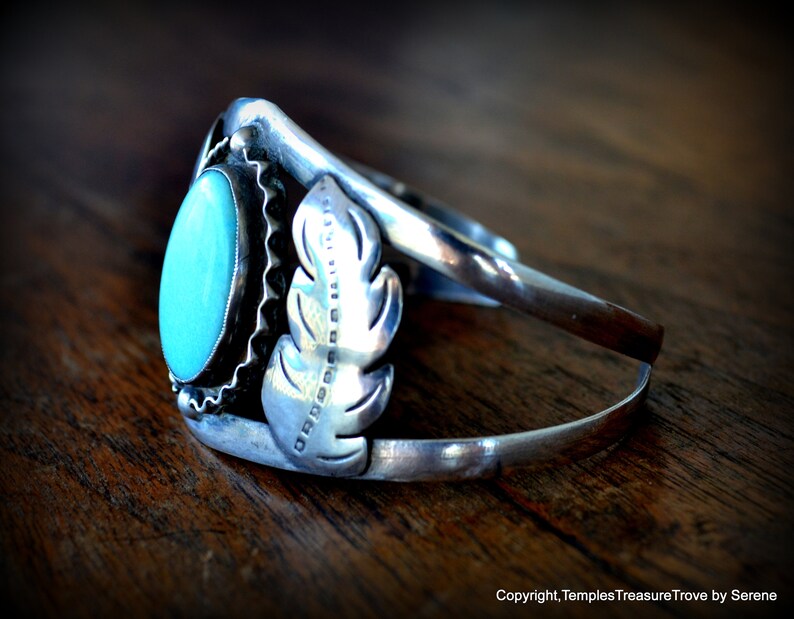 Puede incluir: Un brazalete de plata con una piedra turquesa y un dise&ntilde;o de pluma. El brazalete est&aacute; estampado con "OROBORO" en el lateral.
