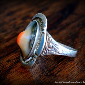 May include: A silver ring with a carved design on the band and a large, oval-shaped, multi-colored stone set in the center.