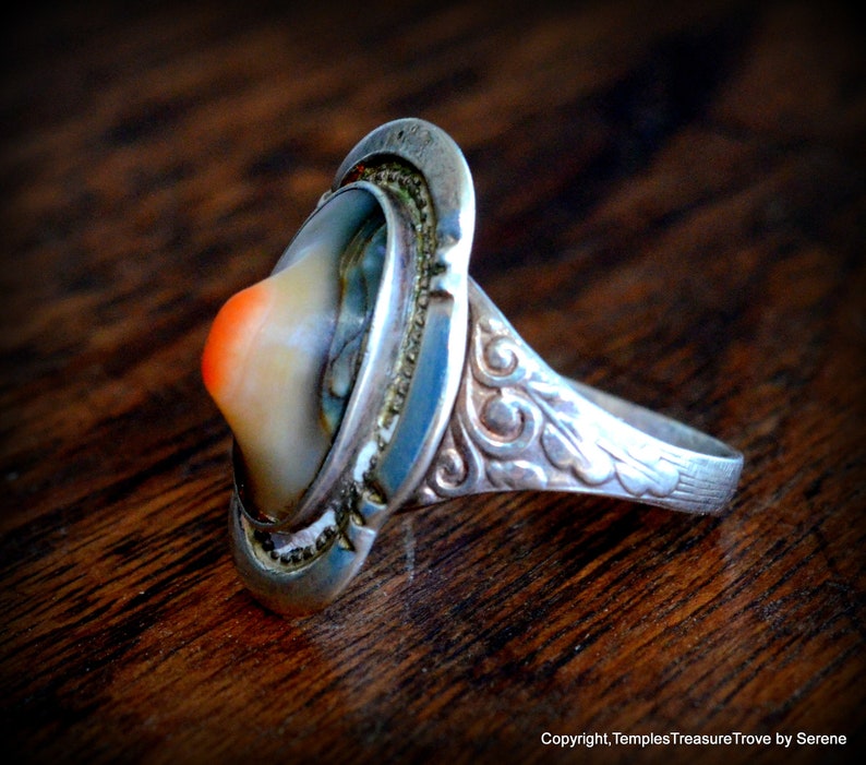 May include: A silver ring with a carved design on the band and a large, oval-shaped, multi-colored stone set in the center.