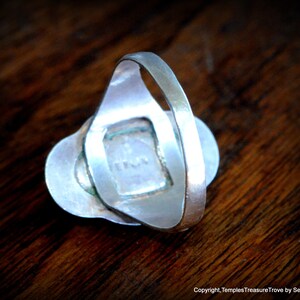 May include: Silver ring with a green stone set in a silver bezel. The ring is on a wooden surface.