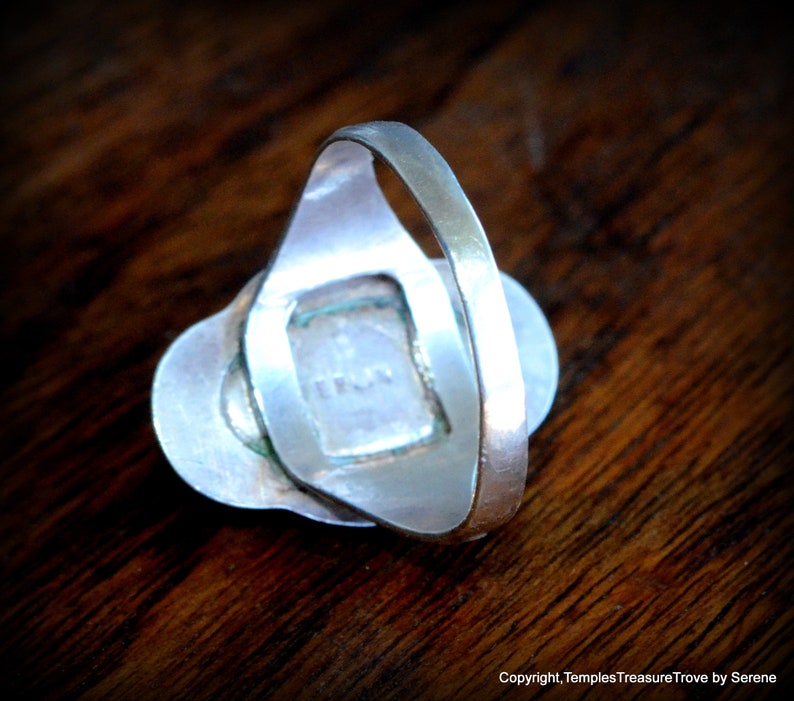 May include: Silver ring with a green stone set in a silver bezel. The ring is on a wooden surface.