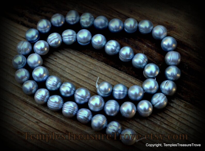 May include: A strand of blue freshwater pearls, strung together on a white cord. The pearls are round and have a smooth, iridescent finish.