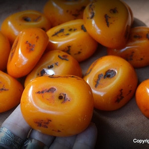 May include: A collection of 10 amber beads with a hole in the center of each bead. The beads are a light orange color and have a glossy finish.