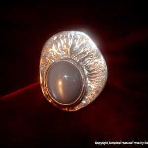 Może przedstawiać: Srebrny pierścionek z fakturowanym wzorem i dużym, okrągłym, szarym kamieniem szlachetnym w środku.