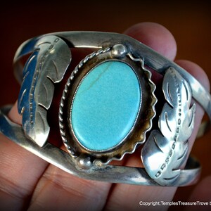 Puede incluir: Un brazalete de plata con una piedra turquesa engastada en un bisel de plata. El brazalete est&aacute; decorado con dos dise&ntilde;os de plumas de plata a cada lado de la piedra.