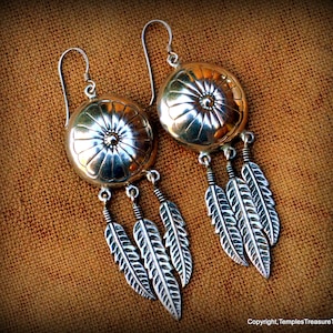 Puede incluir: Pendientes de plata con un diseño circular y plumas colgantes. Los pendientes tienen un patrón texturizado, similar a una flor.