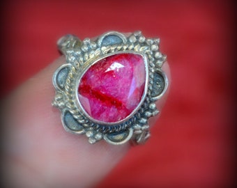 May include: A silver ring with a pink gemstone set in a detailed ornate design.