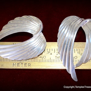 May include: A pair of silver earrings with a fan-shaped design. The earrings are approximately 1 1/4 inches long.