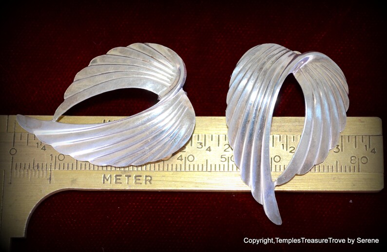 May include: A pair of silver earrings with a fan-shaped design. The earrings are approximately 1 1/4 inches long.