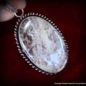 May include: A silver pendant with a clear quartz crystal set in an oval bezel. The bezel has a twisted wire design around the edge.