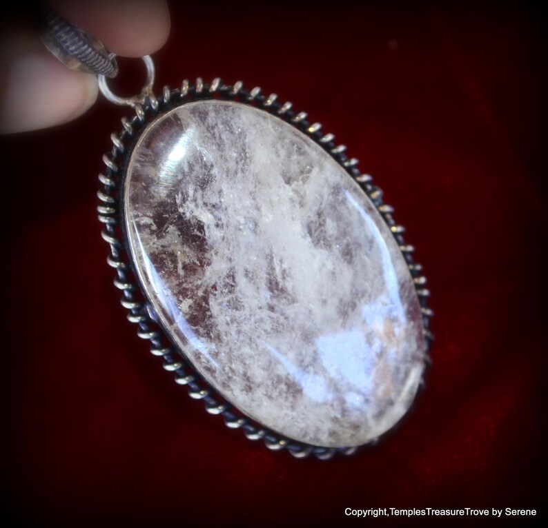 May include: A silver pendant with a clear quartz crystal set in an oval bezel. The bezel has a twisted wire design around the edge.