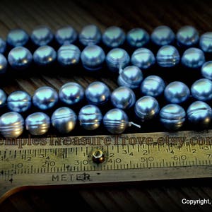 May include: A strand of blue freshwater pearls, measuring approximately 46 cm in length, laid out on a wooden surface with a ruler for size reference.