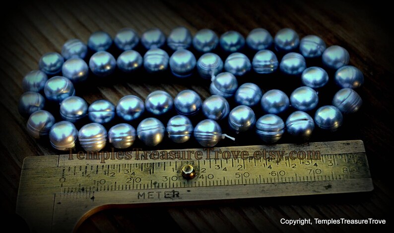 May include: A strand of blue freshwater pearls, measuring approximately 46 cm in length, laid out on a wooden surface with a ruler for size reference.