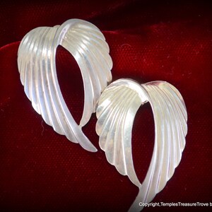May include: A pair of silver earrings with a unique, curved, and textured design. The earrings are shaped like a wing or a leaf.