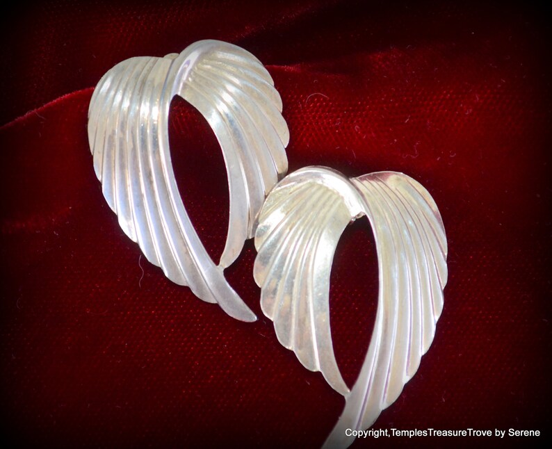 May include: A pair of silver earrings with a unique, curved, and textured design. The earrings are shaped like a wing or a leaf.