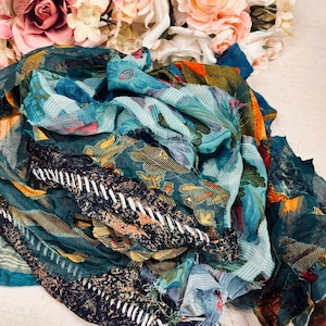 May include: A collection of colorful scarves with floral and abstract patterns. The scarves are in shades of teal, blue, orange, and navy, with white stitched details. A bouquet of pink and white roses is in the background.