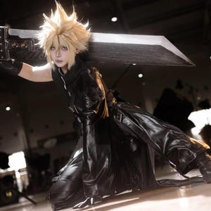 May include: A cosplay outfit featuring a spiky blonde wig and a black leather-like ensemble. The costume includes a long coat, pants, and gloves. A large, silver sword is held across the back, completing the character's look.