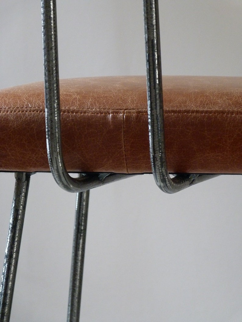May include: Close-up of a brown leather chair seat with a metal frame. The chair has a simple, modern design with thin metal legs.