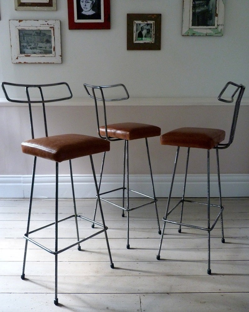 May include: Three metal bar stools with brown leather seats. The stools have a simple, industrial design and are perfect for a modern kitchen or dining room.