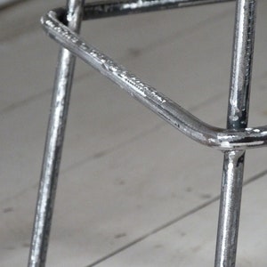 May include: Close-up of a metal bar stool with a silver finish. The stool has a triangular base and a simple design.