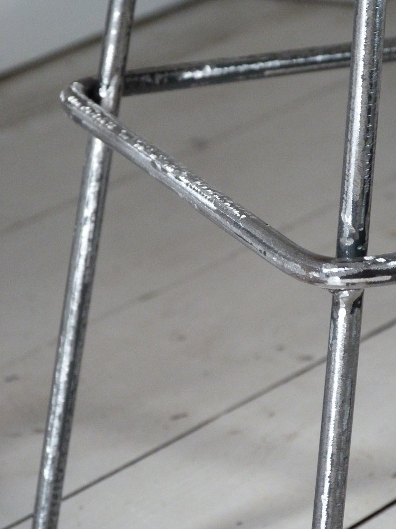 May include: Close-up of a metal bar stool with a silver finish. The stool has a triangular base and a simple design.