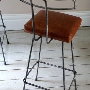 May include: A brown leather bar stool with a metal frame. The stool has a simple, modern design with a curved backrest and a rectangular seat.