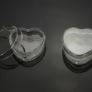 Puede incluir: Dos recipientes de plástico transparente en forma de corazón con tapas. Los recipientes están apilados uno encima del otro.