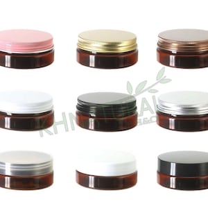 Puede incluir: Diez tarros de vidrio ámbar con tapas de diferentes colores. Las tapas son plateadas, doradas, rosadas, negras y blancas. Los tarros son todos del mismo tamaño y forma.