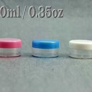 Könnte beinhalten: Drei kleine, transparente Plastikbehälter mit Deckeln. Die Behälter haben ein Fassungsvermögen von 10 ml oder 0,35 oz. Die Deckel sind rosa, blau und weiß.