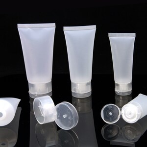 May include: Three clear plastic squeeze bottles with flip-top caps. The bottles are different sizes and are arranged in a row on a black surface.