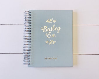 May include: A light blue spiral bound journal with gold lettering that says "Bailey Eve" and "My First Year".