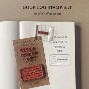 May include: A book log stamp set with five cling mount stamps. The set includes stamps for "Now Reading," "Finished," and "DNF," along with a rating stamp. The stamps are displayed on a notebook page.