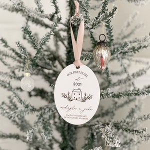 May include: White oval Christmas bauble with the text "Our First Home est 2021" and a small house illustration. Below the house is the text "nickayla & john" and "2140 East Walter Ave Montgomery Alabama".