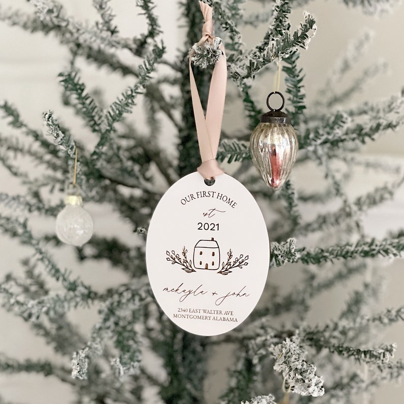 May include: White oval Christmas bauble with the text "Our First Home est 2021" and a small house illustration. Below the house is the text "nickayla & john" and "2140 East Walter Ave Montgomery Alabama".