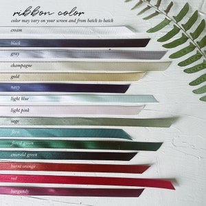 May include: A selection of ribbon colours displayed on a white surface. The colours include cream, black, grey, champagne, gold, navy, light blue, light pink, sage, fern, forest green, emerald green, burnt orange, red, and burgundy.