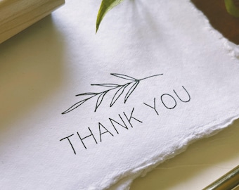 May include: A white card with a simple black line drawing of a branch with leaves and the text "THANK YOU" printed in black.