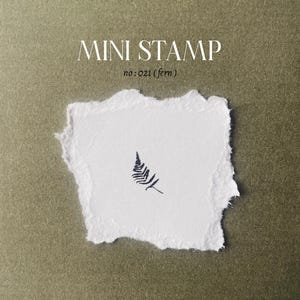 May include: A small, black fern leaf design on a white piece of paper. The paper has a torn edge. The text "MINI STAMP no: 021 (fern)" is printed above the design.