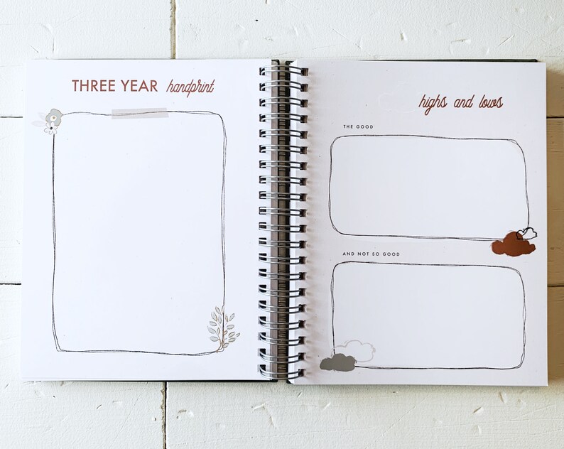 May include: A white journal with a brown spiral binding. The left page has the text "THREE YEAR handprint" and a blank space for a handprint. The right page has the text "highs and lows" and two blank spaces for writing.