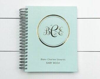 May include: A light blue baby book with a gold circle monogram of "BCE" and the text "Blake Charlee Edwards BABY BOOK".