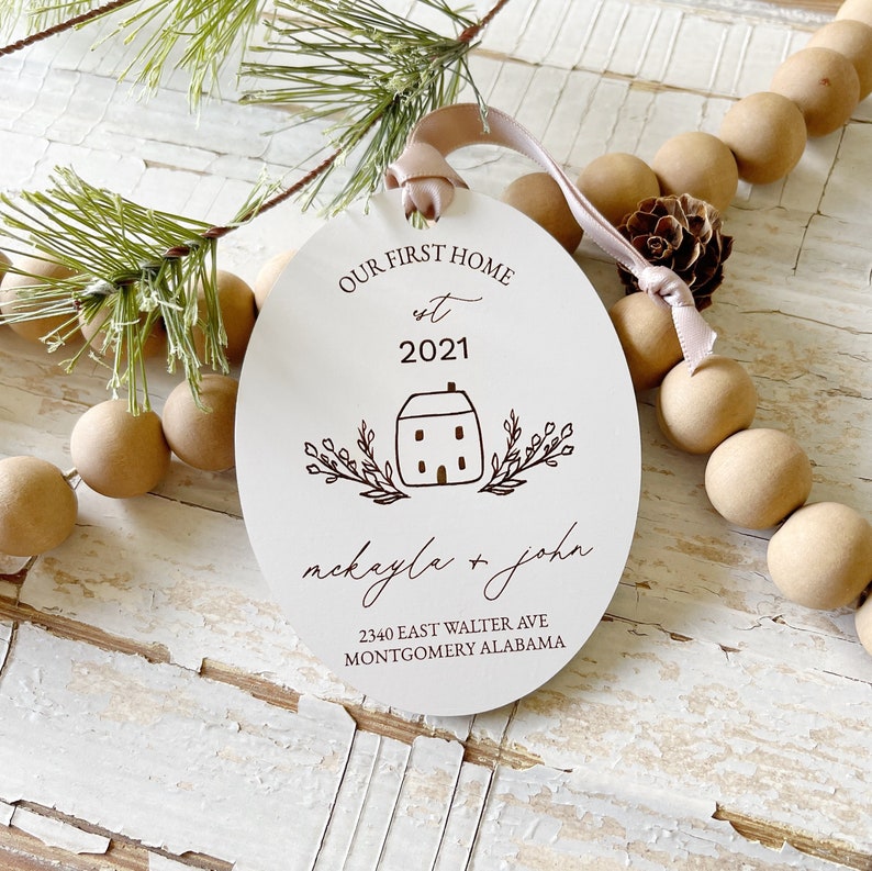 May include: White wooden ornament with the text "Our First Home est 2021" and a small house illustration. Below the house is the text "mackayla + john" and the address "2340 East Walter Ave Montgomery Alabama".