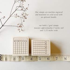 May include: Two wooden stamps with a grid pattern and the days of the week labeled. The stamps measure approximately 2 inches tall and 1.25 inches wide.  The stamps are shown next to a ruler.