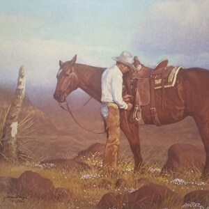 May include: A watercolor painting depicts a cowboy adjusting a saddle on a brown horse in a desert landscape. The cowboy wears a white shirt, chaps, and a hat. The scene is set against a backdrop of rolling hills and a hazy sky, with wildflowers in the foreground.