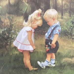May include: A young girl in a white dress with red trim stands in a grassy field. She is looking down at a young boy in a blue and white shirt and black shorts. The boy is wearing white sneakers and has blonde hair. The background is a forest with tall trees.