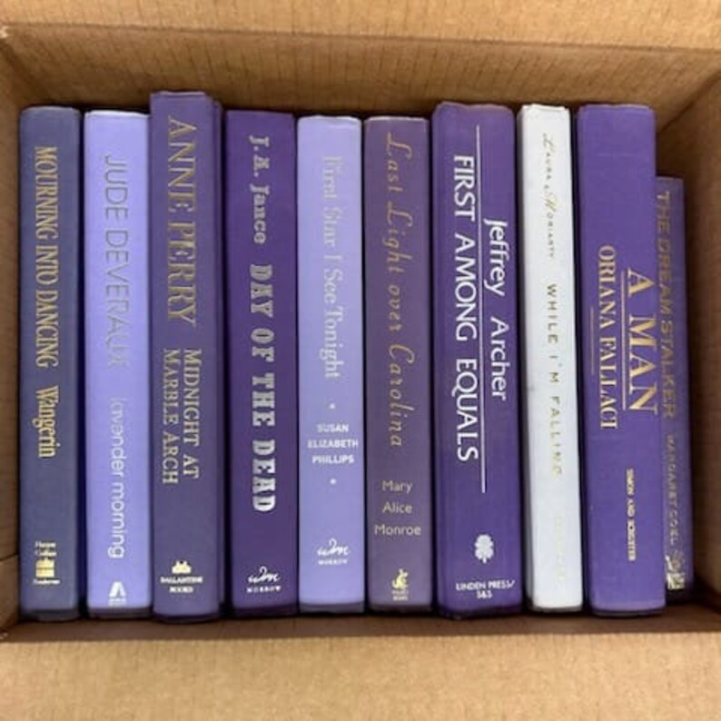 Puede incluir: Una colecci&oacute;n de diez libros de tapa dura de color morado y azul con letras doradas en los lomos. Los libros est&aacute;n dispuestos verticalmente en una fila sobre una superficie marr&oacute;n.