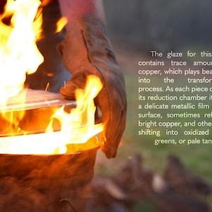 May include: A ceramic vessel being removed from a fire, featuring a glaze with copper that creates metallic films in shades of blue, green, and tan. The text reads: The glaze for this piece contains trace amounts of copper, which plays beautifully into the transformation process. As each piece cools in its reduction chamber it forms a delicate metallic film on the surface, sometimes reflecting bright copper, and other times shifting into oxidized blues, greens, or pale tans.